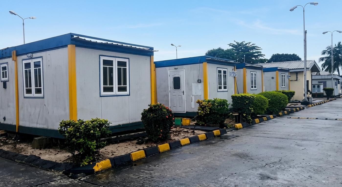 Row of blue-trimmed modular accommodation units along a paved, landscaped walkway