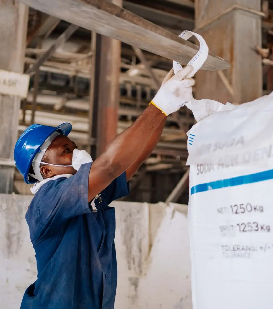 Xtetix worker in a hard hat and dust mask rigging a bulk bag at an industrial facility