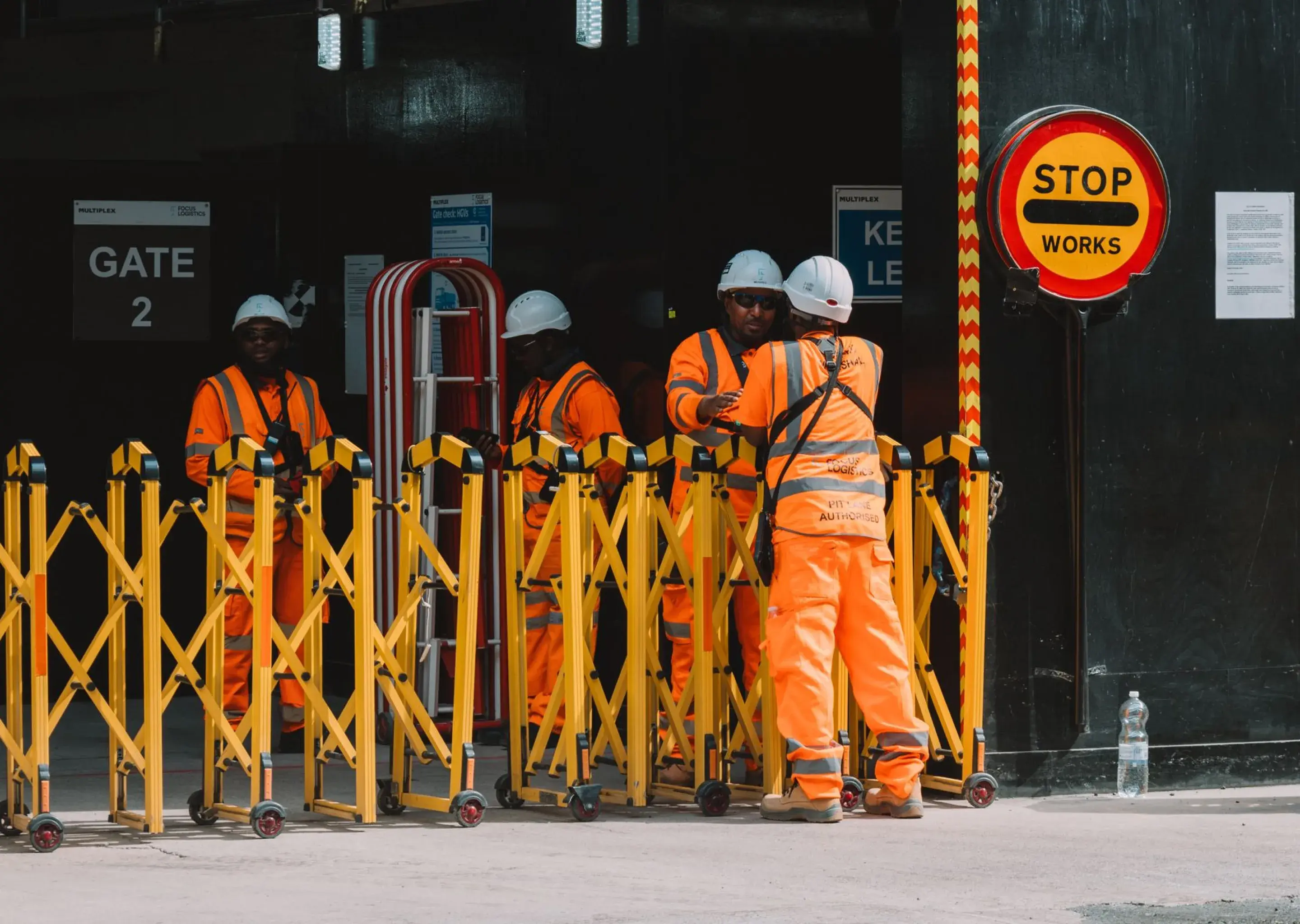 Site crew in high-visibility PPE at a gated works entrance with a stop sign